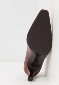 Zapato marrón de tacón con acabado texturizado de patrón de reptil, puntera afilada y suela negra brillante. Tacón vertical para mayor soporte.