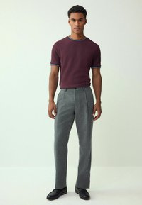 Bordo spalvos trumpomis rankovėmis marškiniai su mėlynais akcentais, derinami su pilkais languotais kelnėmis ir juodais batais, pasižymintys siauru siluetu ir lygiu audiniu.