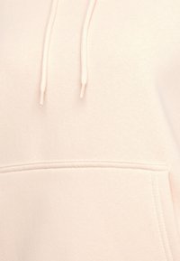 Lichtroze hoodie van zachte stof, voorzien van een buidelzak en koordjes. Gestructureerde oppervlakte met subtiele stiksel details.