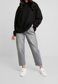 Sudadera negra de gran tamaño, jeans grises y zapatillas blancas. La sudadera tiene mangas largas y un ajuste holgado; los jeans presentan un corte recto.