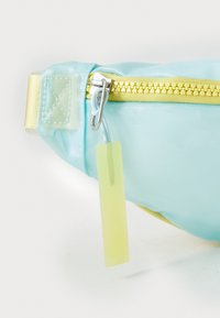 Rucsac de talie de culoare albastră deschisă cu fermoar și accesorii galbene. Are un finisaj lucios, material din nailon texturat și un eticheta din plastic atașată.