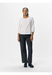 Blusa bianca in pizzo con maniche a tre quarti, scollo rotondo e texture sottile. Abbinata a jeans scuri a vita alta e stivali neri.