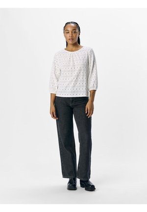 White eyelet blouse with three-quarter sleeves, round neckline, and subtle texture. Paired with high-waisted dark jeans and black boots.
