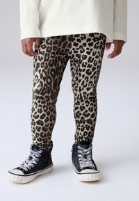 Leggings con estampado de leopardo en tonos verdes y beige, combinados con zapatillas altas de color azul marino que presentan cordones blancos con el logo y una suela en contraste.