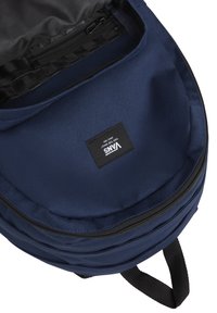 Mörkblå ryggsäck i hållbart tyg med rundad form, med en svart dragkedja och innerfack; varumärkesetikett synlig inuti.