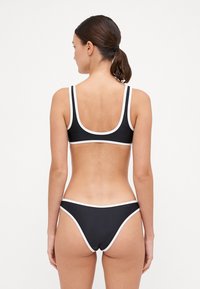 Ensemble de bikini noir comprenant un haut à décolleté plongeant et un bas taille basse avec des bordures blanches contrastées. Tissu lisse et extensible offrant une couverture minimale.