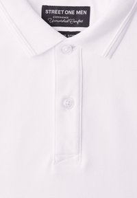 Polo blanc pour hommes avec deux boutons et une étiquette noire portant l'inscription « STREET ONE MEN Experience Unmatched Comfort » au niveau du col.