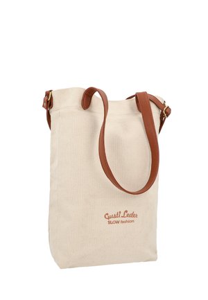 Beige Leinwandtasche mit braunen Lederriemen und „Gusti Leder SLOW fashion“ auf der Vorderseite bedruckt.