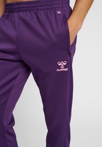 Paarse sportbroeken gemaakt van soepele stof, met een elastische tailleband, zijzak en een roze logo op de dij.