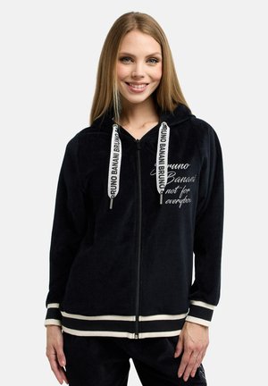 Zwarte velours zip-up hoodie met witte trekkoorden, voorzien van een bedrukte slogan en gestreepte accenten bij de manchetten en zoom.