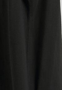 Tissu de robe en coton noir avec une texture douce, présentant une surface lisse et un détail de couture verticale, capturant un design minimaliste.