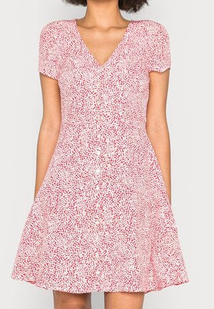 Femme portant une robe rouge et blanche à manches courtes, col en V avec des boutons sur le devant et une jupe évasée.