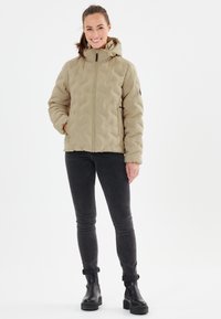 Beige quiltad pufferjacka med huva, frontdragkedja och sidofickor, matchad med svarta slim-fit jeans och svarta ankelstövlar.