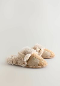 Béžové pantofle s načechraným kožíškem, akcenty z tkaniny s herringbone vzorem a ozdobným prošíváním. Kulatá špička a design na přezouvání.