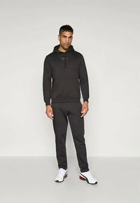 Fekete kapucnis pulóver zsinórral és elülső zsebbel, párosítva fekete melegítőnadrággal. Fehér sportcipő piros és fekete akcentusokkal.