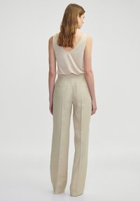 Beige linnen broek met een hoge taille en wijde pijpen, gecombineerd met een lichtbeige V-hals tanktop. Stof lijkt zacht te zijn met minimale afwerking.