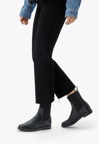 Botas de cuero negras hasta el tobillo con paneles elásticos laterales, punteras redondeadas y suela plana. Combinadas con jeans negros cortos y una chaqueta de mezclilla.