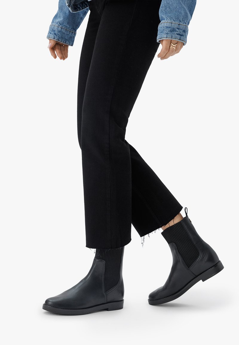 Botas de cuero negras hasta el tobillo con paneles elásticos laterales, punteras redondeadas y suela plana. Combinadas con jeans negros cortos y una chaqueta de mezclilla.