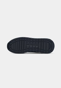 Semelle de chaussure en caoutchouc noir avec un motif de bande de roulement texturé, comportant des rainures horizontales et verticales pour une traction et une adhérence accrues.