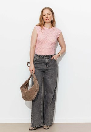 Femme portant un haut en dentelle rose transparente, un jean gris taille haute à jambes larges, des chaussures à imprimé léopard, tenant un sac à main marron avec des œillets dorés.