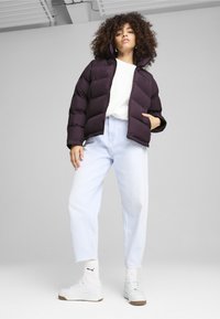 Lilla pufferjakke med høj krave, parret med lyseblå baggy jeans og hvide sneakers. Glat tekstur, lynlåslukning og logodetalje.