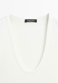 White V-neck shirt neckline with a black "Massimo Dutti Made in China" label sewn on the inside back collar.