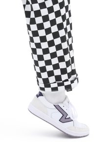 Sneakers bianchi con un accento viola, tessuto testurizzato, abbinate a pantaloni a scacchi in bianco e nero, con orlo arrotolato e etichetta con logo.