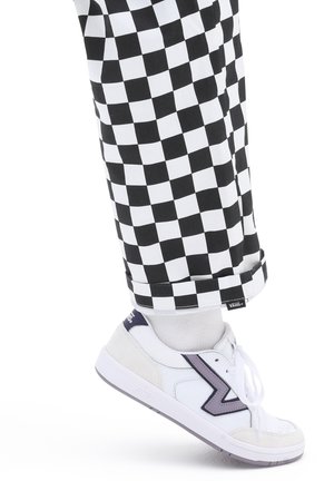 Sneakers bianchi con un accento viola, tessuto testurizzato, abbinate a pantaloni a scacchi in bianco e nero, con orlo arrotolato e etichetta con logo.