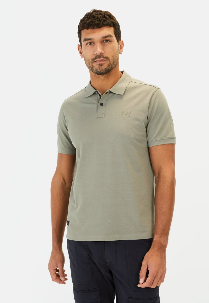 Grågrøn polo-shirt lavet af glat stof, med en placket med tre knapper og et lille logo på brystet. Bæres med mørke cargo shorts.