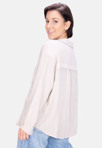 Light beige, textured button-up shirt with a relaxed fit, collar, and back yoke detail; worn with blue denim jeans.