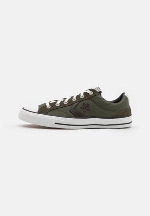 Lage olijfgroene sneaker met witte veters, zwart sterlogo, witte rubberen zool en zwart streepdetail op een effen achtergrond.
