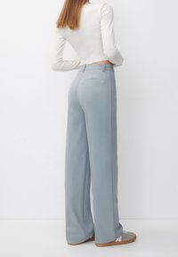 Pantalones de pierna ancha en azul claro con una textura suave, pliegues en la parte delantera y un ajuste entallado. Combinados con una blusa blanca de manga larga ajustada.