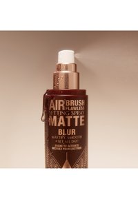 Maroon bottle with gold text. White spray nozzle at the top. The bottle shows droplets of water and has geometric patterns on the base.