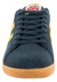 Sneaker in suede navy con righe gialle, punta rotonda e suola in gomma marrone. Presenta un'etichetta con logo raffigurante la bandiera dell'Union Jack sulla linguetta.