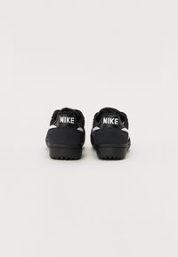 Sorte Nike sneakers med en tekstureret overdel, hvide accenter på siderne og stort hvidt logo på hælen. Tykk gummisål med trækmønster.