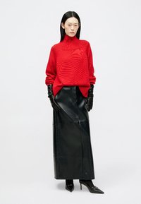 Piros kötött pulóver magas nyakkal, hosszú fekete bőrszoknyával párosítva. Fekete bőrgumik és hegyes fekete talpú cipők egészítik ki a szettet.