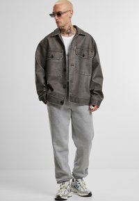 Gray denim jacket with two patch pockets, button closure, and contrast stitching. Paired with gray sweatpants and multi-colored sneakers.