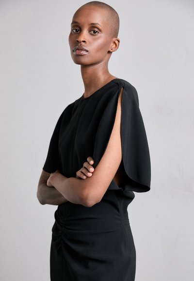 Rochie neagră cu mâneci scurte tip capa, având o guler înalt, detaliu plisat pe lateral și un design asimetric cu partea laterală deschisă. Textură netedă a materialului.