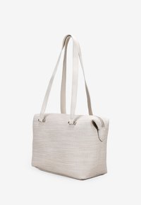 Bolso tote de color beige, tejido con tela texturizada y asas de cuero liso, que cuenta con un cierre de cremallera y un bolsillo lateral. Forma rectangular.