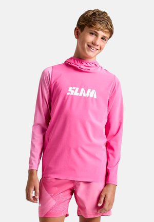 Teen boy smiling, wearing a bright pink long-sleeve top with "SLAM" text and matching pink shorts, standing against a light background.