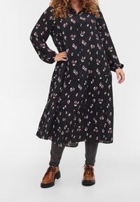 Svart klänning med krage och långa ärmar, med ett blommönster i vitt och rosa. Designen inkluderar lager på lager vid fållen.