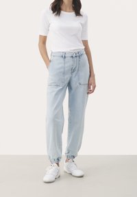 Jasnoniebieskie dżinsowe joggery z dwoma przednimi kieszeniami, elastycznymi mankietami i pasem ze sznurkiem, w zestawie z dopasowaną białą bluzką z krótkim rękawem.