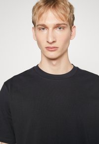 Tricou negru cu guler rotund, fabricat dintr-un material de bumbac neted; prezintă un design simplu și clasic, cu o ușoară întindere și fără modele vizibile.
