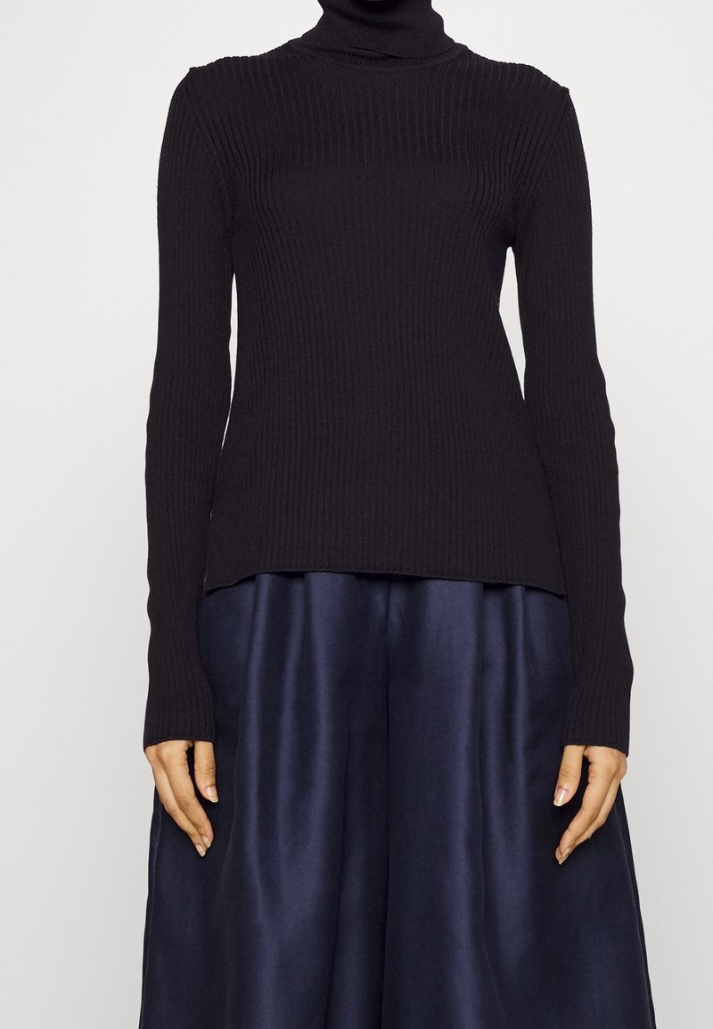 Pull à col roulé noir côtelé à manches longues, en tissu tricoté. L'ourlet est droit et légèrement plus long à l'arrière.