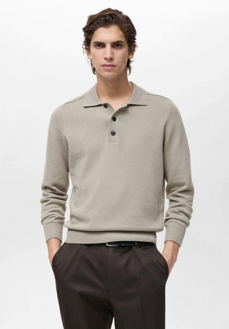 Beige knitted polo shirt with a collared neckline, three black buttons, and ribbed cuffs. Paired with dark trousers for a classic look.
