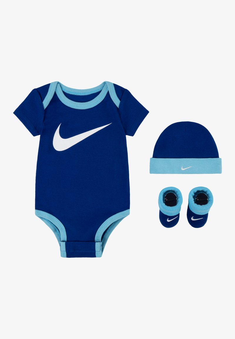 Grenouillère en coton bleu avec des bordures bleu clair, ornée d'un grand logo Nike blanc. Comprend un bonnet assorti et des chaussons, également en bleu.