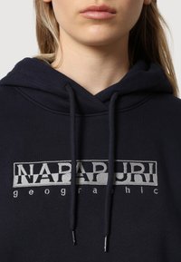 Granatowy sweatshirt z kapturem, wyposażony w sznurek do regulacji, kangurzą kieszeń oraz kontrastowe, haftowane logo na klatce piersiowej w kolorze szarym. Miękka tekstura materiału.