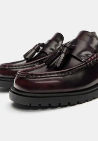 Bordeaux leren loafers met kwastaccenten, gestikte details en een dikke zwarte rubberen zool, met een glanzende afwerking en ronde vorm.