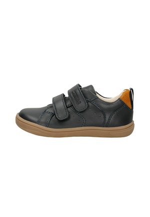 Zapatilla negra de niño con dos tiras de velcro, suela marrón y detalle naranja en la lengüeta del talón, vista lateral sobre fondo blanco.
