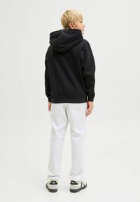 Felpa nera con cappuccio regolabile, abbinata a pantaloni della tuta grigi chiari. L'outfit presenta polsini a coste e una vestibilità casual.